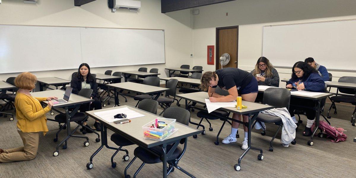 Judy is kneeling while she assists students in the Project Success class